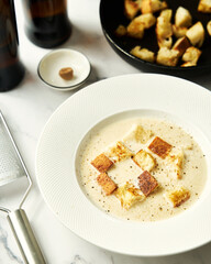 Beer soup with bread croutons and nutmeg. There are bottles of beer, croutons and a grater next to them. White background