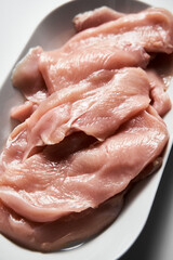 Raw Chicken fillet cut into schnitzel on an oval platter on a white marble kitchen countertop
