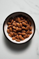 Roasted Almonds in the bowl on white marble kitchen countertop. Top view
