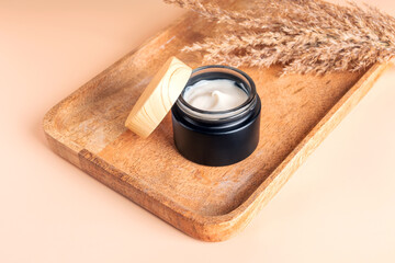 face cream on wooden tray on beige background. Dry ear reeds or pampas grass decoration....