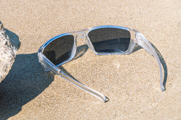 The beach on the river bank. Sunglasses in a white transparent frame are lying on the beach. Sand on the beach. Summer holidays on the river bank. Protection from the sun.