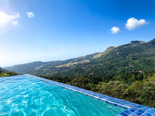 Infinity pool overlooking jungle valley with mountains in the background on a bright beautiful blue day