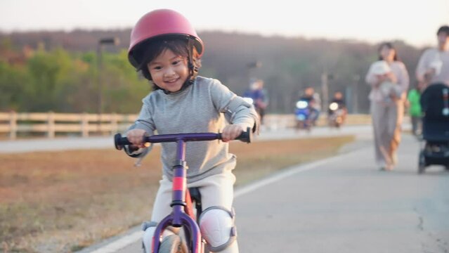 Joyful asian female toddler riding a bike along the roadside, playful and fun children, moving activities for puberty development, body and mind coordination, happy asian girl ride bicycle.
