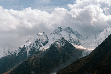 View of snow-covered mountain peaks in the clouds on a sunny autumn day