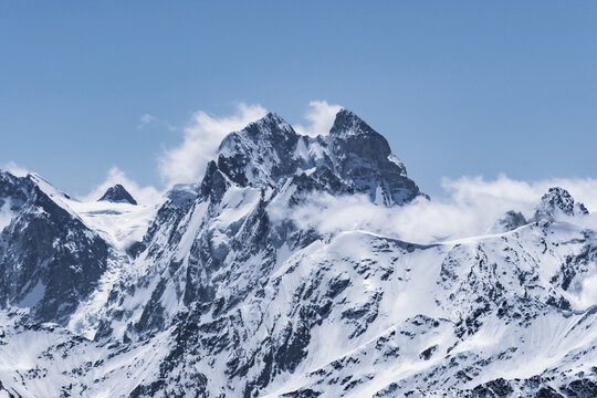 View of Mount Ushba and snow-covered peaks on a cloudy day from the top of Mount Elbrus