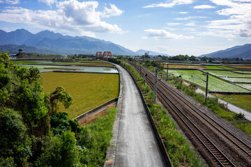 Fototapeta na wymiar View of the countryside in spring around Yuli Taiwan from above. Green rice fields, train tracks, blue sky and the famous red old railway bridge