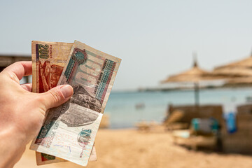 Egyptian pounds in a man's hand on the background of the beach. Egyptian money - obrazy, fototapety, plakaty