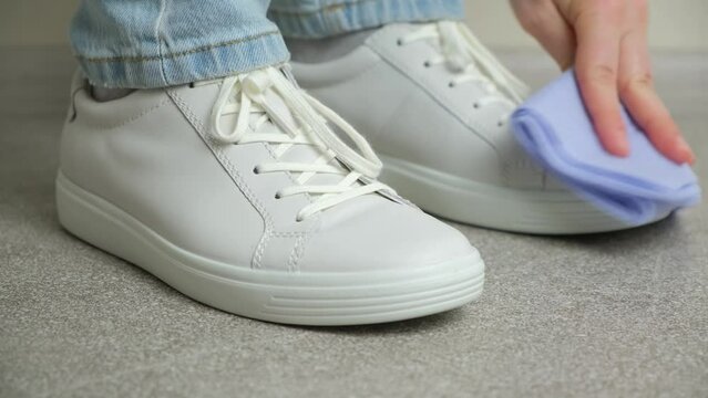 A woman cleans white leather sneakers with a rag, removes dust, takes a step forward
