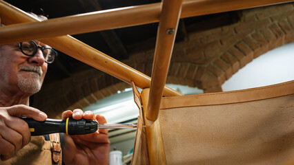 tanner screwing the leather parts to a chair made by hand in a small shop in rome center....