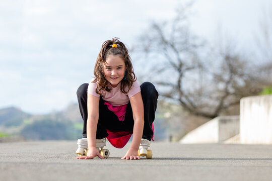 Smiling cute girl sitting on road while skating with roller skates