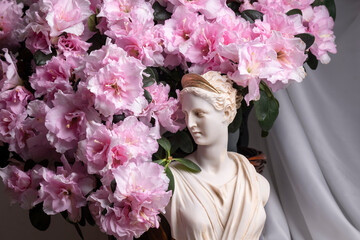 Still life of female divinity sculpture and flowering azalea flower 