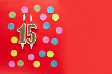 Number 15 on a red background with colored confetti. Happy birthday candles. The concept of...
