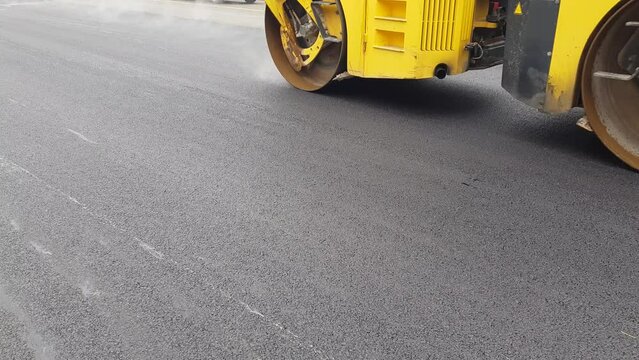 A large asphalt road roller, a vibrating roller that moves and compresses the freshly laid asphalt base, road infrastructure reconstruction