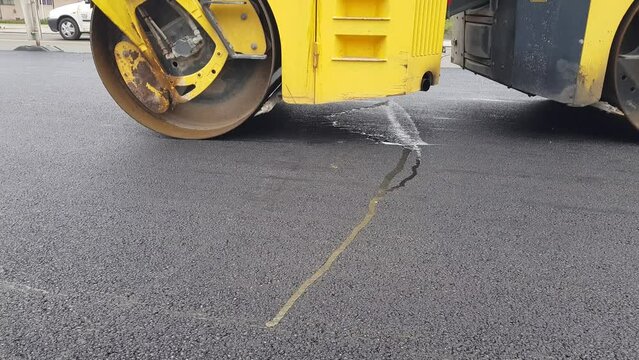 A large asphalt road roller, a vibrating roller that moves and compresses the freshly laid asphalt base, road infrastructure reconstruction