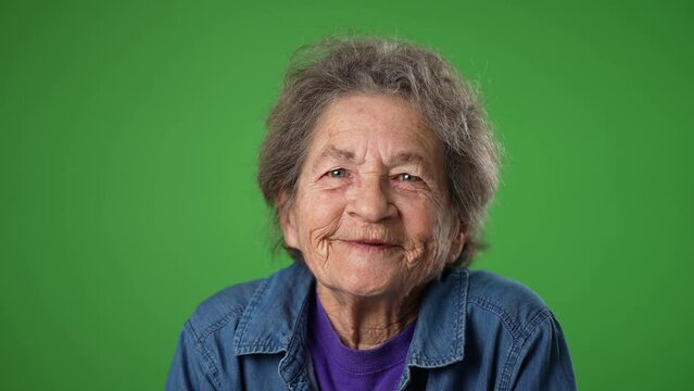 Closeup slow motion portrait of smiling happy toothless elderly senior old woman with wrinkled skin and grey hair isolated on green screen background in studio. Emotions concept