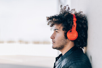 handsome young North African man in casual clothing listens to music with headphones, looking dreamy