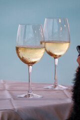 Two glasses with white wine on the table and part of the hand of a girl in black clothes holding a mobile phone.