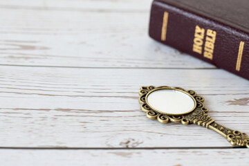 Ancient golden mirror and closed holy bible book on wooden table. Christian biblical concept of...
