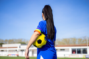 Soccer player woman with a soccer ball and captain armband with the LGBT pride flag on the field. Campaign against homophobia in football. LGBTQ people in sport concept. Women's Football.