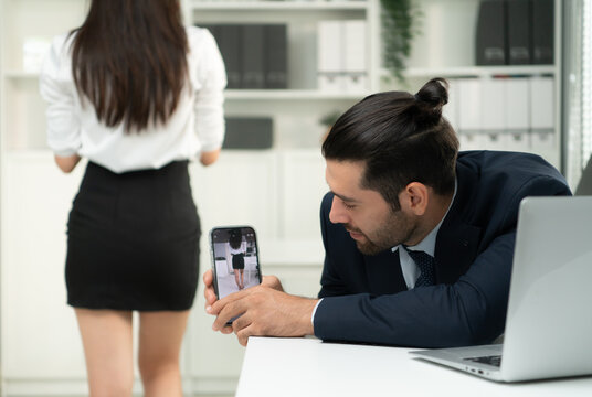 An executive is secretly using a phone to take a picture of an employee's buttocks in the company with emotional feelings and preferences. The concept of harassment and sex in the office.