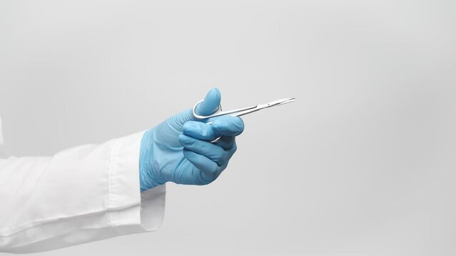 Cropped shot of a doctor's hand in a blue glove holding scissors for manicure, makes cutting gesture. 4k, slow motion, close up.