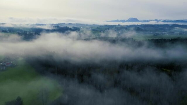 Impressive drone hyper-lapse shot of the foggy Upper Austrian alpine foothills with Traunstein mountain in the background. Camera moves backwards through the patches of fog.