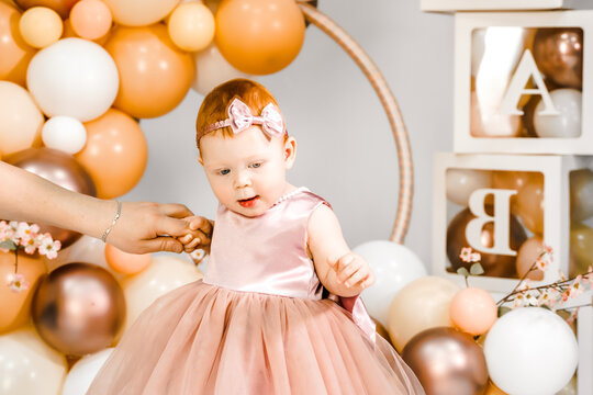 Little redhead baby girl celebrates first birthday anniversary. 1 year family baloons party. Professional photoshoot. Photo studio. Cute adorable red hair kid. Red holiday dress. Children's home room