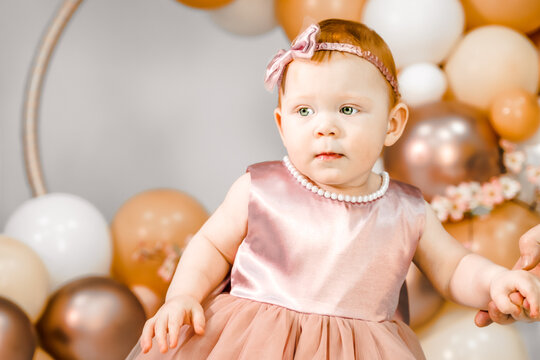 Little redhead baby girl celebrates first birthday anniversary. 1 year family baloons party. Professional photoshoot. Photo studio. Cute adorable red hair kid. Red holiday dress. Children's home room