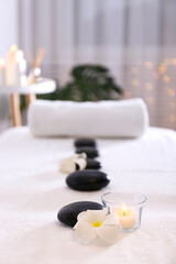 Close up shot of black volcanic stones laid in line and a rolled towel on the massage table in a spa salon room. Bokeh lights on the background. Copy space.