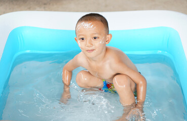 Hot weather. Boy playing with water happily in the tub.