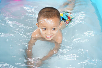 Hot weather. Boy playing with water happily in the tub.