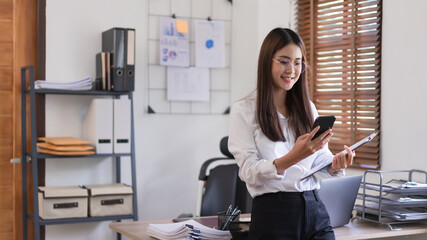 Business concept, Businesswoman holding clipboard and stand to reading business data in smartphone