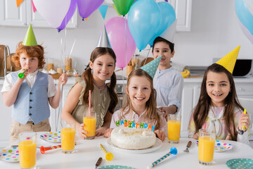 group of happy kids celebrating birthday party next to cake with candles at home.