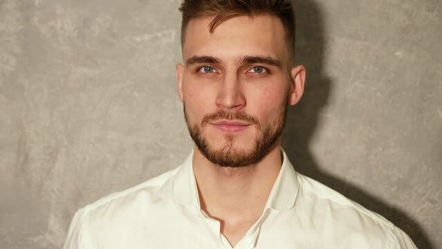Portrait of attractive bearded stylish young man looking into the camera and smiling. Model wearing white summer clothes