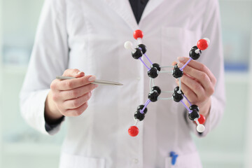 Woman in lab coat demonstrates molecule model in hands