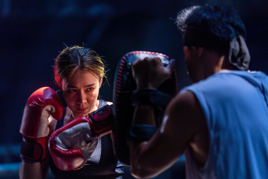 Female kickboxing training with male trainer gives self-defense classes to female fighter at GYM. Asian beautiful young woman exercise with trainer at boxing gloves, uppercut short, boxing, training