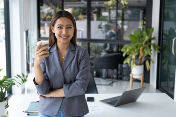 Young pretty businesswoman having a coffee break, smiling and holding a coffee cup in the office room.