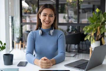 Portrait of young beautiful woman smiling and sitting at her desk, working with laptop computer.