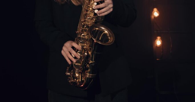 Young girl playing saxophone against a black background. Close-up. Cinematic view