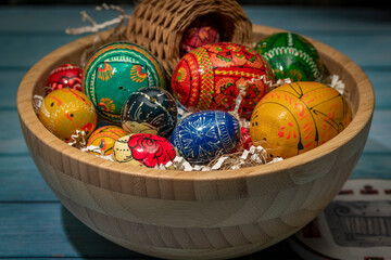 Color easter eggs in light wooden bowl on blue old wooden table