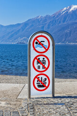 Sign on the shore of Lago Maggiore restricting swimming, sunbathing and bringing food - 592323573
