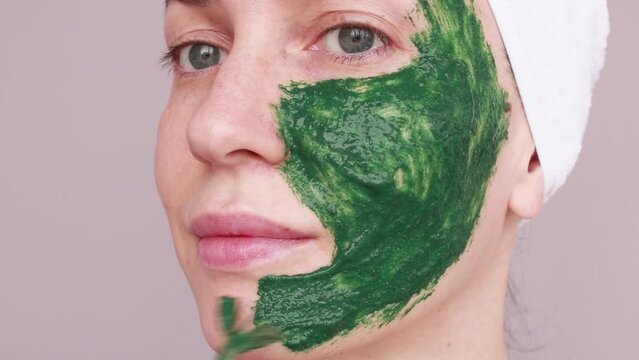 A young woman applies a green mask to her face with a brush. Facial skin care at home. Homemade face mask.