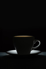 Silhouette of a mug with a warm drink on a black background. Morning coffee.