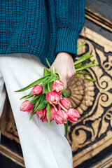 No face close up of pink tulips flowers bouquet in female hand outdoors. Unrecognizable woman holding in hands a bouquet of pink tulips