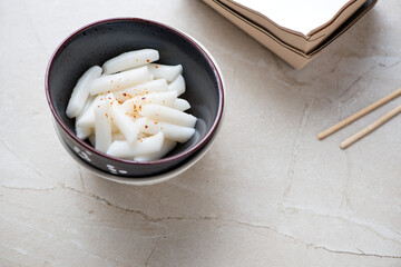 Black bowl with garaetteok or korean traditional street food and snack, horizontal shot on a beige stone background