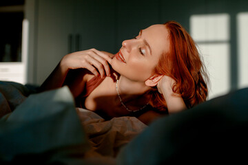 Portrait of a pretty young girl on a bed in a modern apartment. She keeps her eyes closed and looks satisfied
