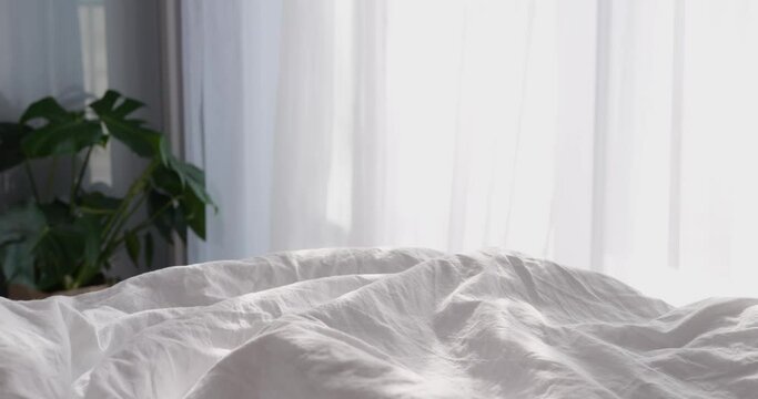White cotton blanket on bed in bedroom at window on bright sunny day. Pleasant and cozy spring or summer morning atmosphere on early start of new day