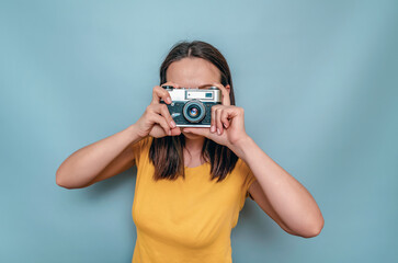 A woman takes pictures with an old film camera. Yellow boot cap, black hair, blue background