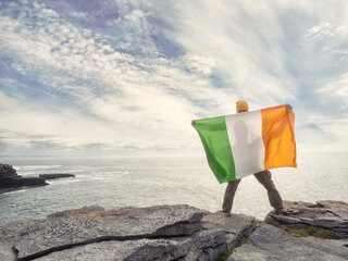 Person holding National flag of Ireland standing on the edge of a cliff, Aran island, county...