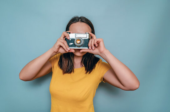A woman takes pictures with an old film camera. Yellow boot cap, black hair, blue background